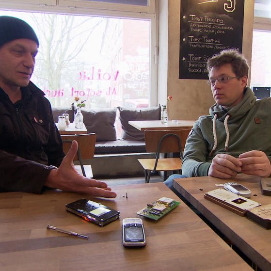 Zwei Männer an einem Tisch, vor ihnen selbst gebaute Handys. (Foto: SWR – Screenshot aus der Sendung)