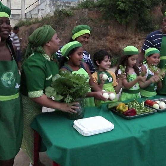 Kinder und Erwachsene, grün gekleidet, stehen um einen Tisch mit Gemüse.
