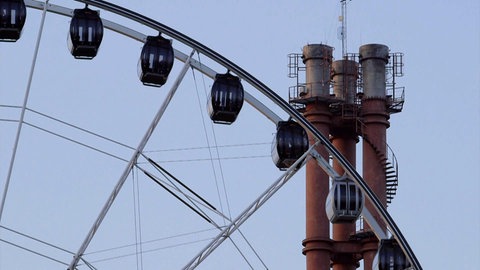 Ein Ausschnitt eines Riesenrads vor einem Industrieschornsteins