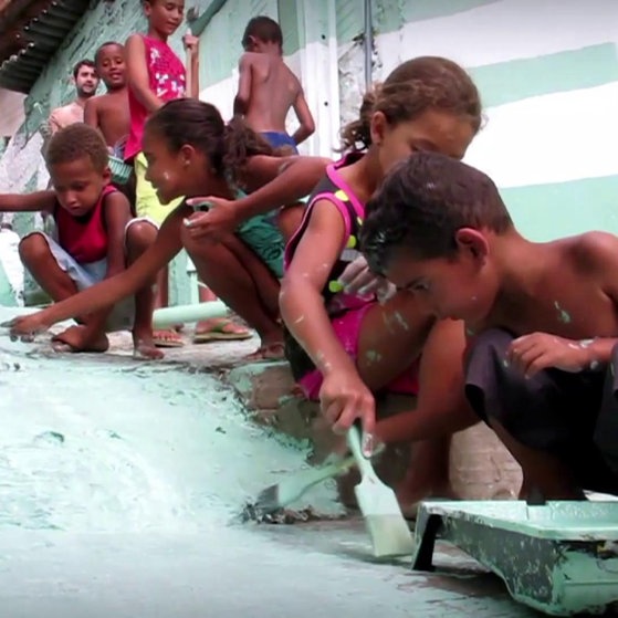 Kinder malen mit Pinseln und Farbrollen einen Weg türkis an.