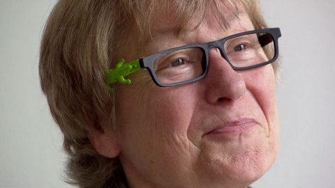Frau mit Brille, auf dem Bügel ein grünes Krokodil.