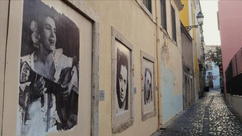 Eine schmale Gasse mit großen Bildern von Personen an der linken Hauswand.