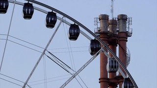 Ein Ausschnitt eines Riesenrads vor einem Industrieschornsteins