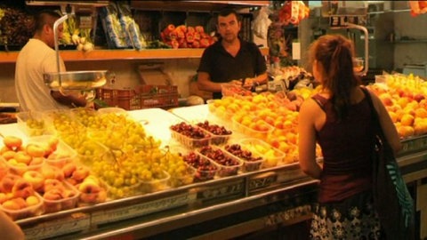 Eine junge Frau steht vor einem Obststand.
