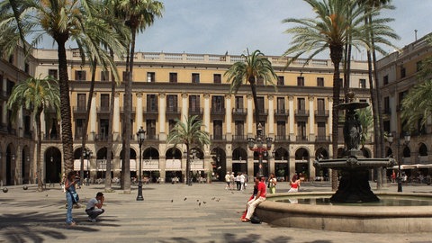 Ein Platz in Barcelona mit einem Brunnen und Palmen.