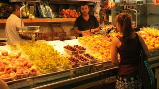 Eine junge Frau steht vor einem Obststand.