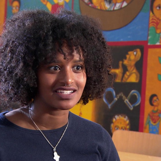 Tezebit vor bunten Bildern mit christlichen Motiven.