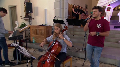 Jugendliche mit Musikinstrumenten in einer Kirche.
