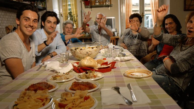 Menschen sitzen an einem gedeckten Tisch und lachen. (Foto: WDR/UR)