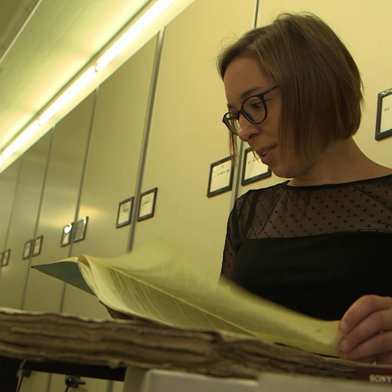 Junge Frau steht vor Aktenschrank und sichtet Akten