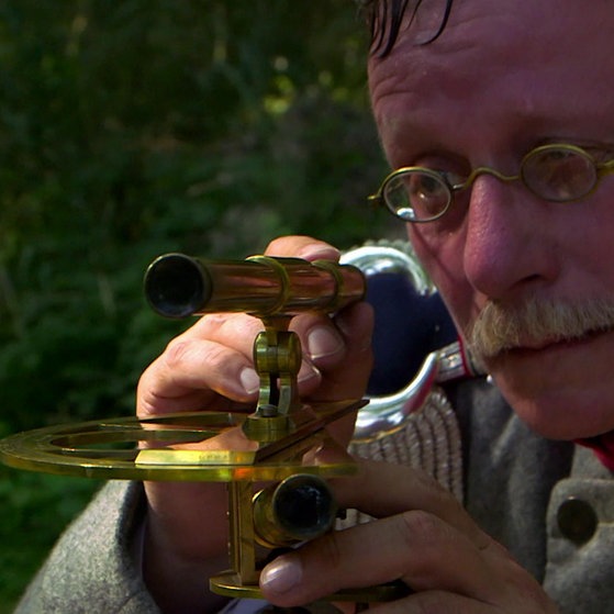 Ein Schauspieler verkörpert Tulla, der am Rhein steht und Messungen durchführt