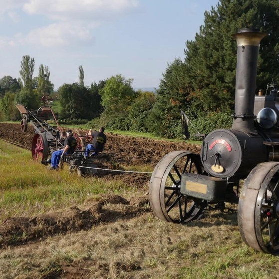 Männer führen mit einem alten Lokomobil das Pflügen auf dem Feld vor.