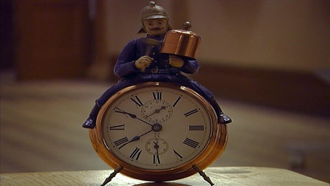 Besonderer Wecker der Firma Junghans: Ein Arbeiter sitzt auf dem Wecker