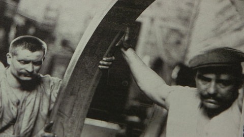 Archivbild: Zwei Arbeiter drehen ein schweres Rad