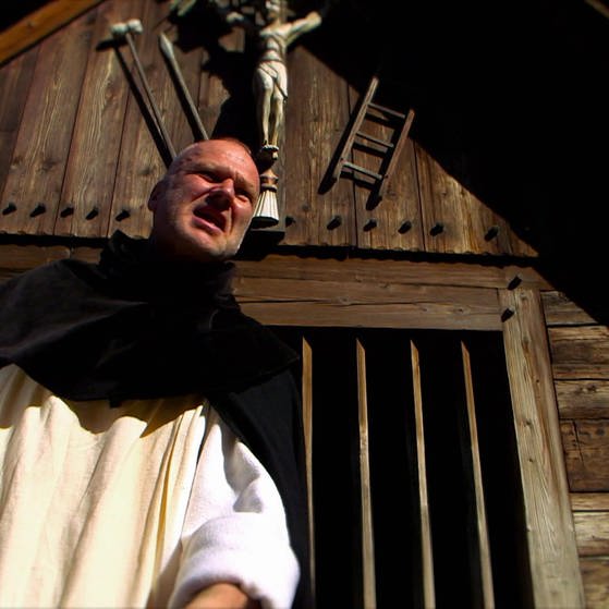 Pfarrer vor Holzgebäude. (Foto: SWR – Screenshot aus der Sendung)
