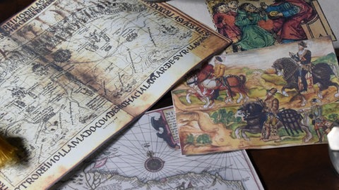 Eine Landkarte und mehrere Zeichnung liegen ausgebreitet auf einem Tisch.