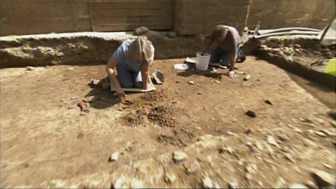 Zwei Archäobotaniker mit kleinen Schaufeln und Eimer auf der Erde. (Foto: SWR/WDR – Screenshot aus der Sendung)