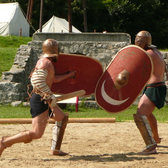 Zwei Männer, wie römische Gladiatoren gekleidet, kämpfen mit Schild und Schwert.