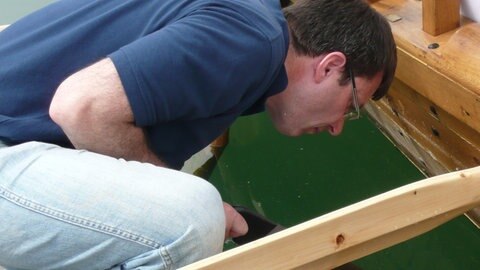Ein Mann beugt sich vor dem nachgebauten Römerschiff ans Wasser.