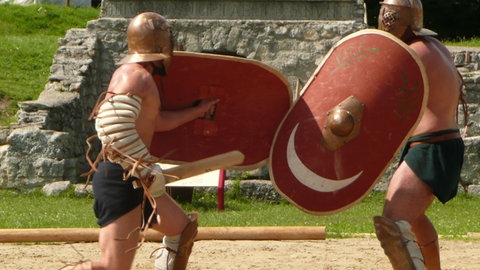 Zwei Männer, wie römische Gladiatoren gekleidet, kämpfen mit Schild und Schwert.