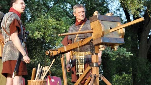 Filmszene: Vier römische Soldaten mit einem hölzernen Pfeilgeschütz.