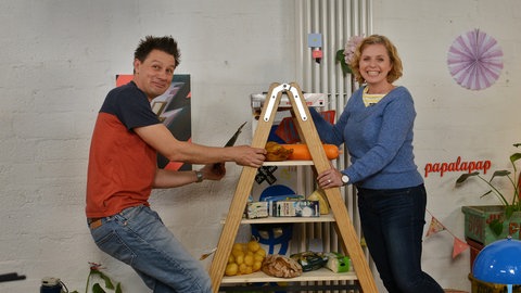 Moderator André Gatzke und die Lehrerin Frau Fobbe stehen an einer Leiter.
