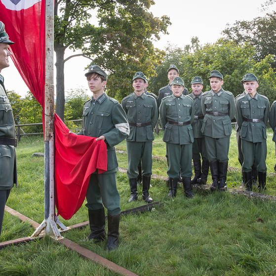 Soldat vor Jungen in Uniform. Dazwischen eine rote Fahne. (Foto: LOOKSfilm/Andreas Wünschirs)