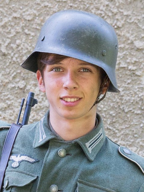 Ein Jugendlicher in Uniform und Soldatenhelm. Auf der Uniform ist ein Zeichen der NSDAP gestickt. (Foto: LOOKSfilm/Andreas Wünschirs)