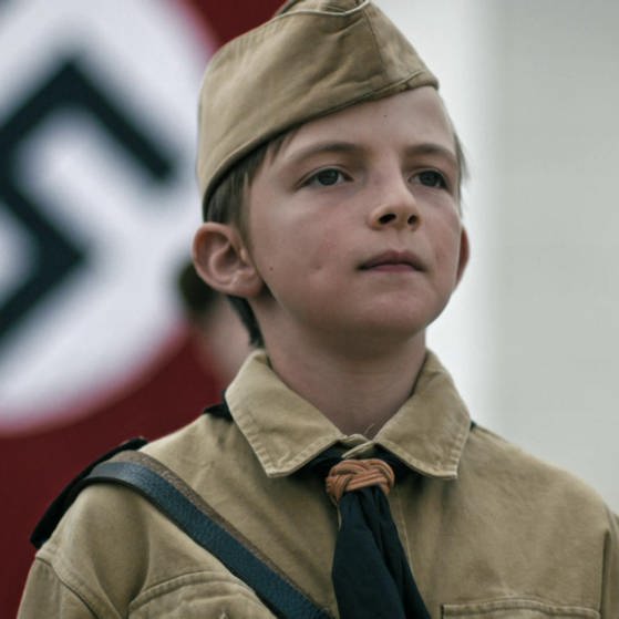 Ein Junge steht in Uniform vor einer Hakenkreuzflagge. (Foto: SWR – Screenshot aus der Sendung)