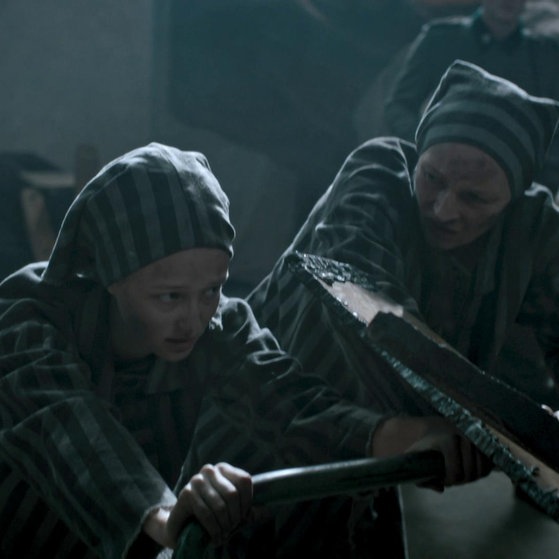 Zwei Frauen in Häftlingskleidung schieben schwer.