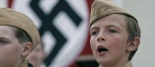 Zwei Jungen in Uniform stehen vor einer Hakenkreuzflagge.