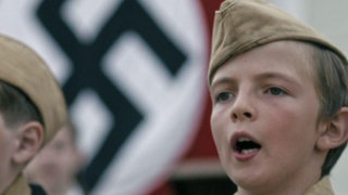Zwei Jungen in Uniform stehen vor einer Hakenkreuzflagge.