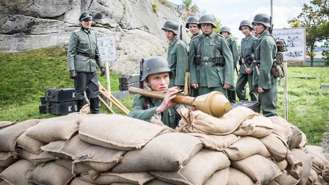 Jungen in Uniform, ein Junge liegt mit Panzerfaust hinter Sandsäcken.