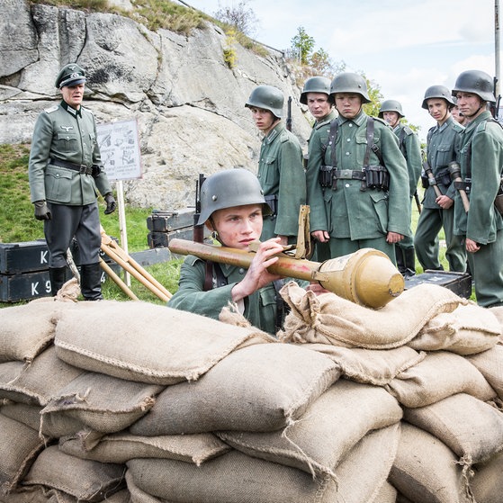 Jungen in Uniform, ein Junge liegt mit Panzerfaust hinter Sandsäcken.