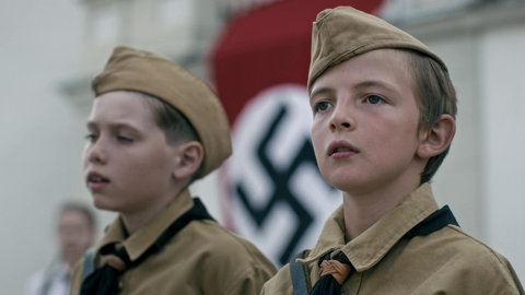 Zwei Jungen in Hitlerjugend-Uniform, im Hintergrund die Hakenkreuzfahne.