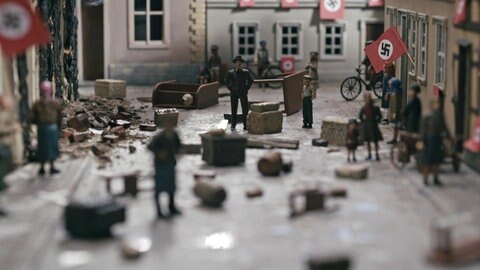 Modellwelt im Film: Zerstörungen an Häusern, überall hängen Hakenkreuz-Fahnen.