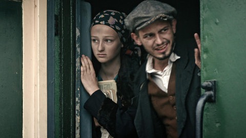 Die Darsteller von Eva und Tomasz schauen aus einer Zugtür.