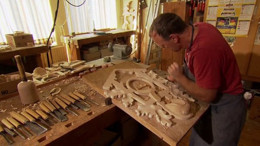 Handwerker schnitzt das Eichenlaub auf der Vorderseite einer Kuckucksuhr