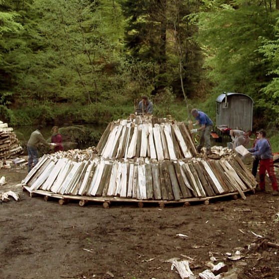 Männer stapeln Holzscheite zu einem  runden Meiler. (Foto: SWR – Screenshot aus der Sendung)