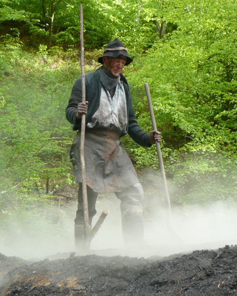 Köhler steht auf dem Meiler und klopft die Erde  fest.