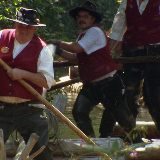 Mehrere Männer steuern und treiben ein Boot an.