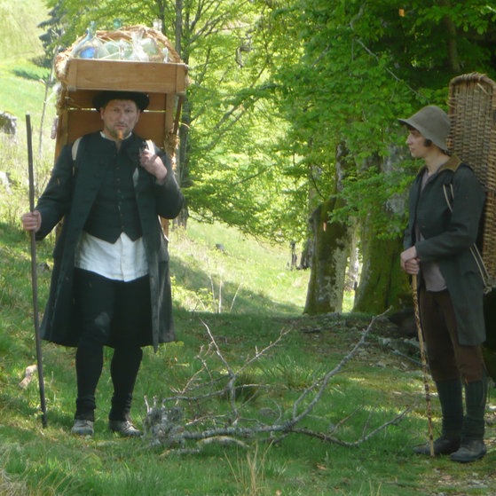 Glasträger mit Holzgestell mit Glaswaren auf dem Rücken; sein Begleiter trägt einen Korb auf dem Rücken.