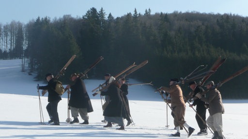 Eine Gruppe von Ausflüglern stapft durch den Schnee, mit Stöcken und geschulterten Skiern