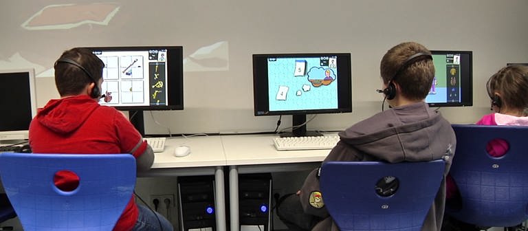 Drei Kinder sitzen mit dem Rücken zur Kamera vor Computern und spielen das Lernspiel Deutsch lernen mit Mumbro und Zinell.  (Foto: SWR / Planet Schule)
