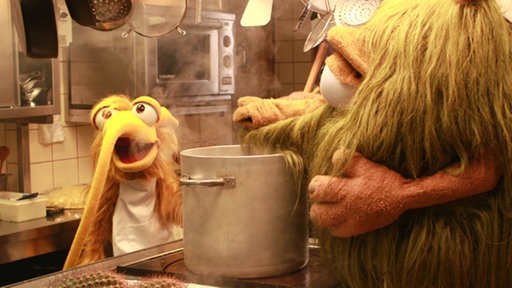 Mumbro (rechts) und Zinell in einer Restaurantküche am Kochtopf. Auf einem Brett liegt ein aufgeschnittener Kaktus.
