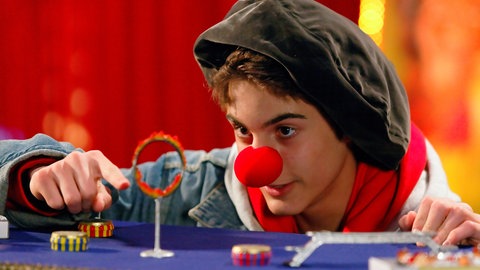 Junge mit roter Clownsnase führt einen Flohzirkus vor.