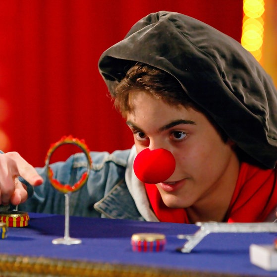 Junge mit roter Clownsnase führt einen Flohzirkus vor.