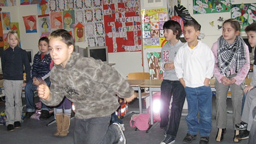 Eine Schulklasse steht im Kreis. Ein Junge beginnt in der Mitte des Kreises zu rennen.