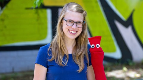 Lernen zusammen deutsch: Esther und die rote Socke sitzen nebeneinander vor einer grünen Wand.