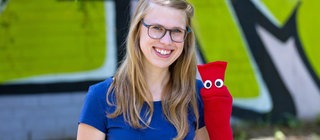 Lernen zusammen deutsch: Esther und die rote Socke sitzen nebeneinander vor einer grünen Wand.